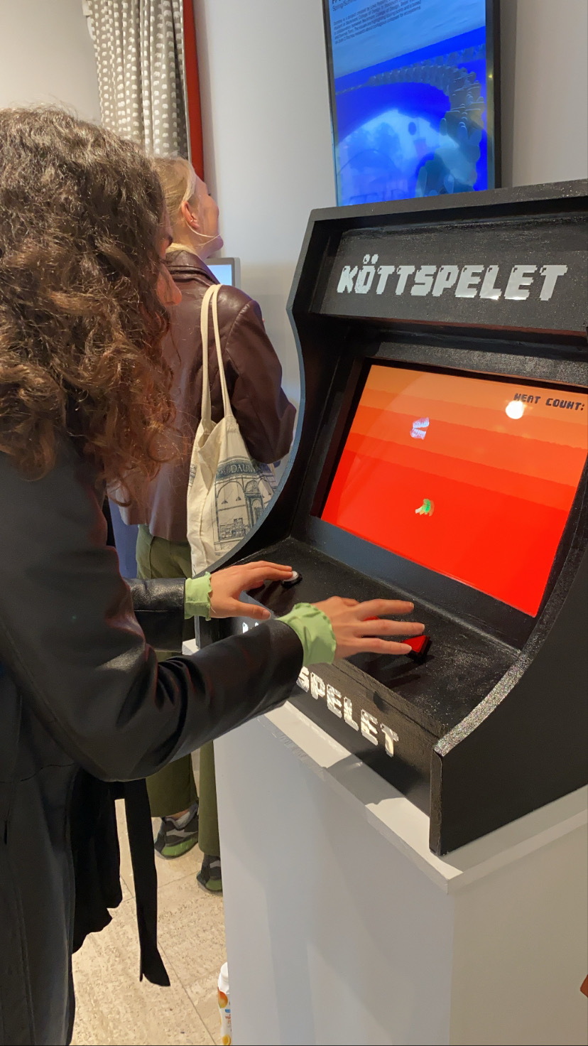 A visitor playing Köttspelet on the arcade cabinet at the exhibition