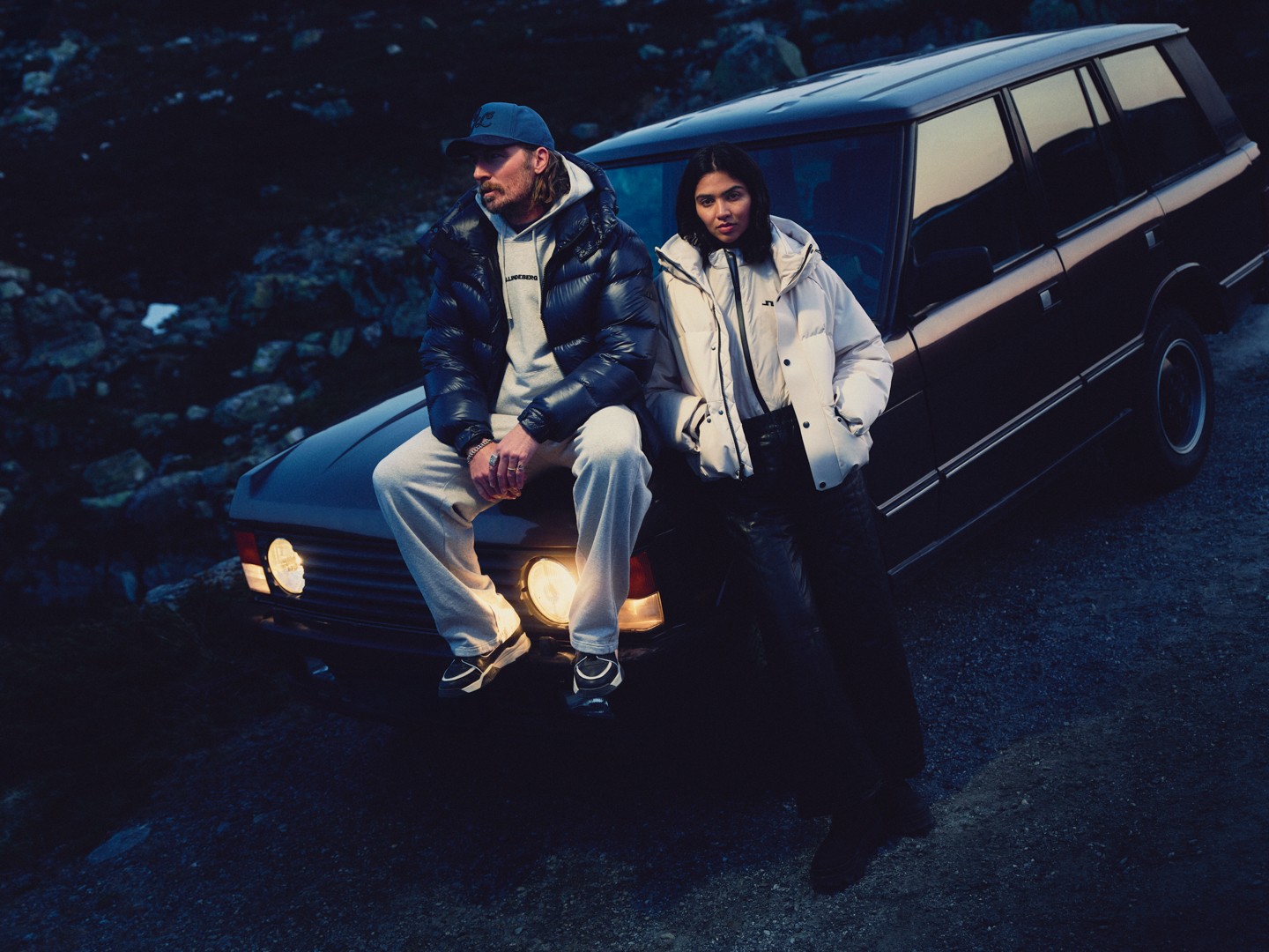 Man and woman in J.LINDEBERG puffer jackets on the bonnet of a classic car at dusk