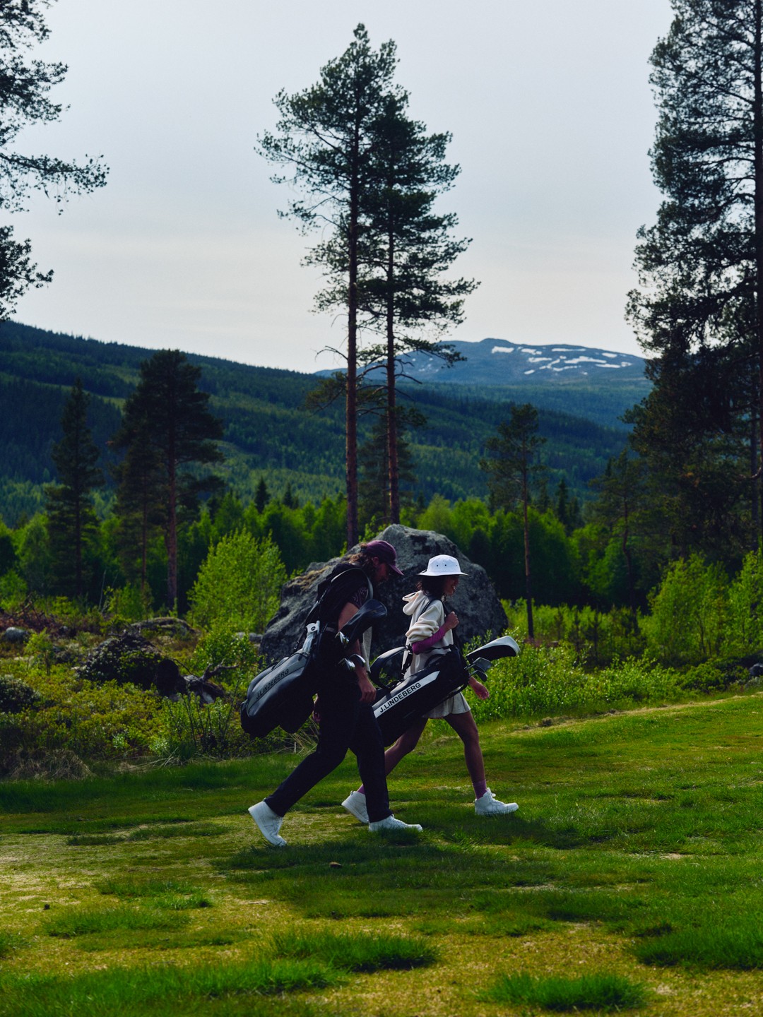 Two golfers carrying J.LINDEBERG bags across a mountain course