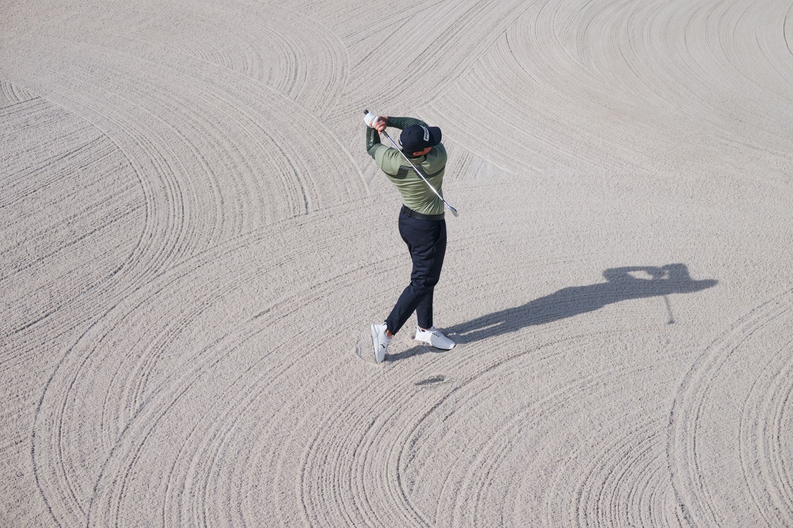 Golfer swinging in a raked bunker, seen from above