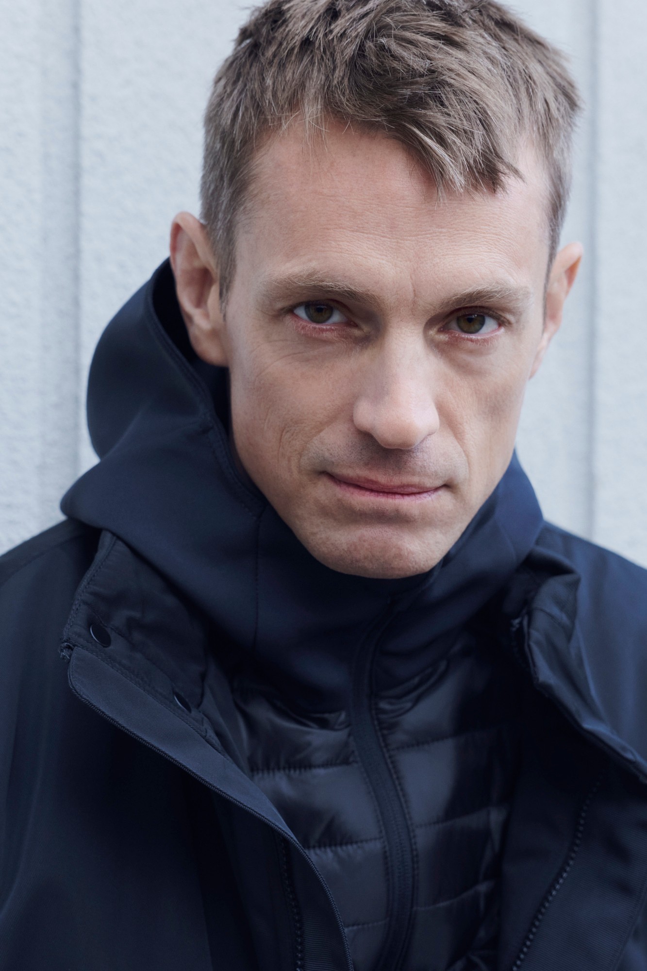 Close-up portrait of Joel Kinnaman in a navy hooded jacket