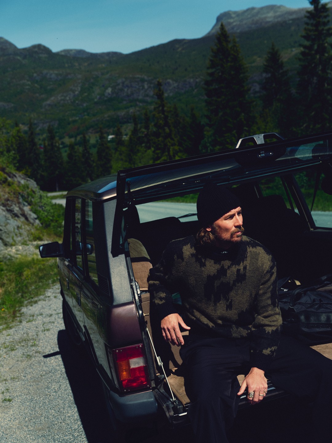 Man in a camouflage-pattern knit sitting in the open boot of a classic car